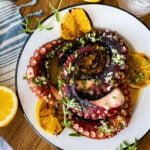 plated easy grilled octopus recipe perfectly grilled on a plate with grilled lemons and dressing. The octopus is slightly charred.