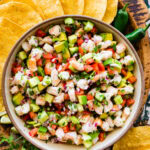 Shrimp ceviche in a bowl surrounded by tortillas and jalapenos.