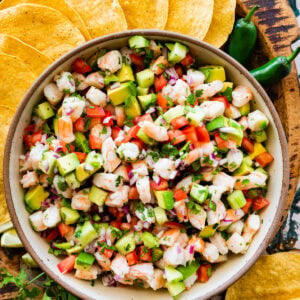 Shrimp ceviche in a bowl surrounded by tortillas and jalapenos.