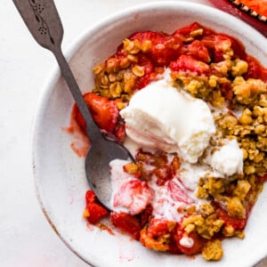 Spoon in a bowl of strawberry crumble with ice cream.