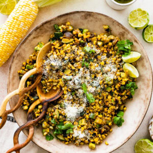 a small bowl of the charred corn and zucchini salad with lime on the side and Serving spoons in a bowl of charred corn and zucchini salad with lime and cilantro.