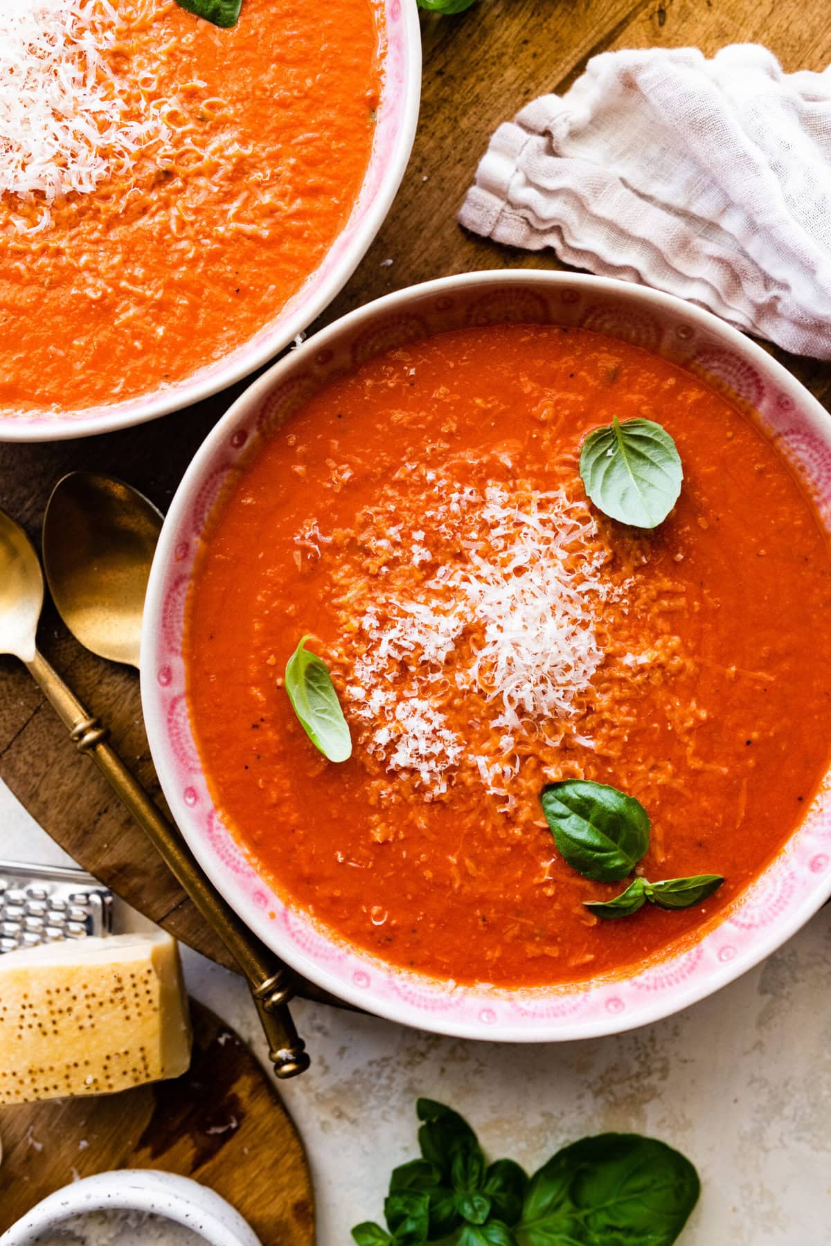 two bowls of creamy tomato soup with basil on top.