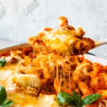 cheese pull with a wooden spoon getting a portion of the meatless baked ziti.