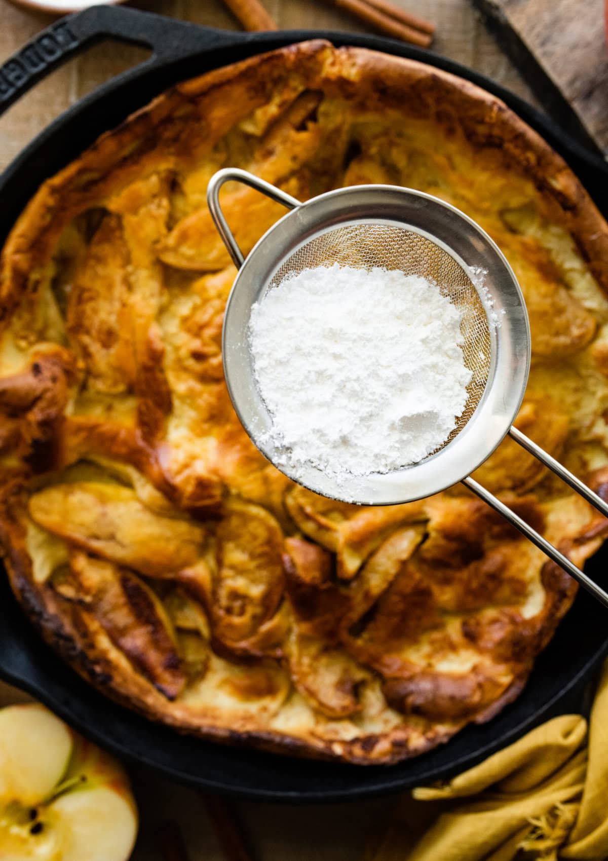 adding powdered sugar to the cooked German Apple Pancake.