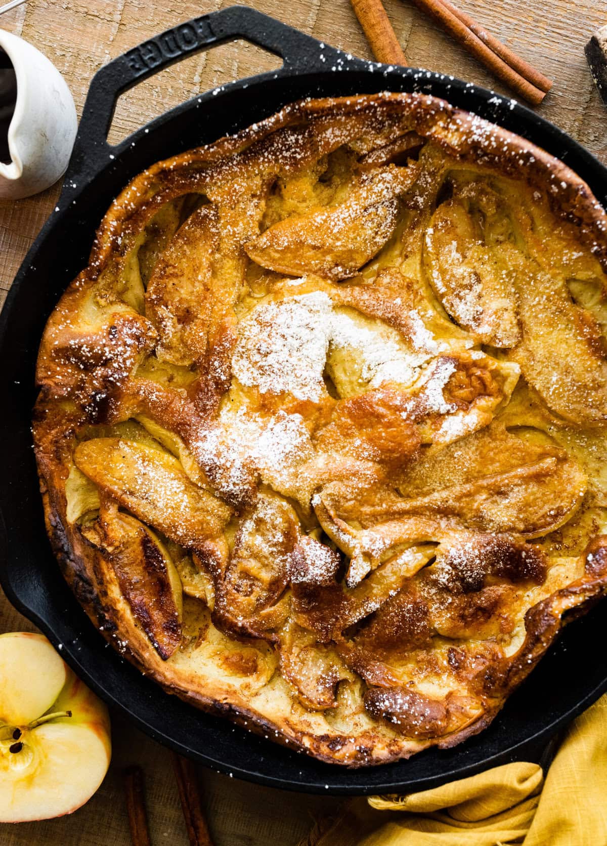 German apple pancake in the cast iron pan with apples and cinnamon sticks around it.