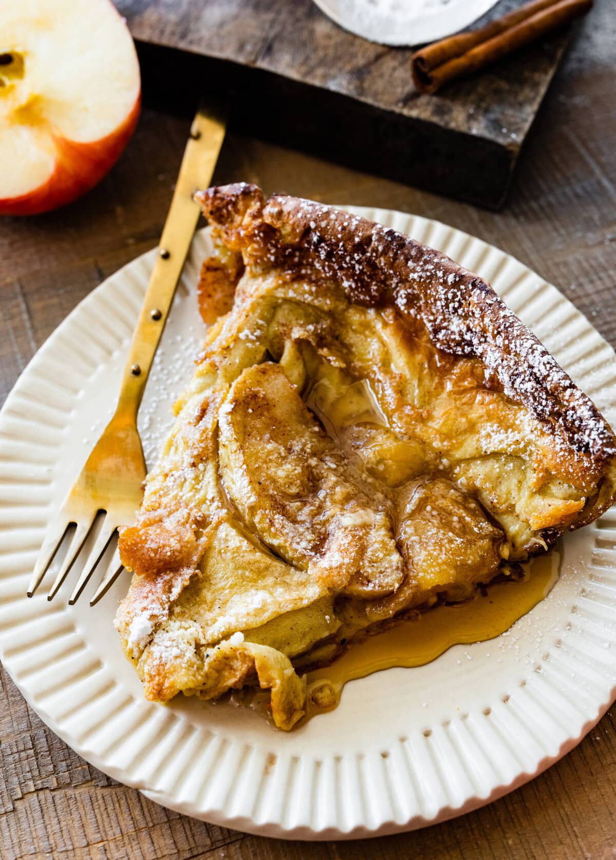 a slice of the apple dutch baby pancake on a white plate with a gold fork ready to eat.