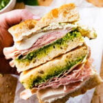 Assembled Mortadella Sandwich Recipe with Pistachio Pesto and Burrata with pesto on the side. Ready to eat. Hands holding the sandwiches.