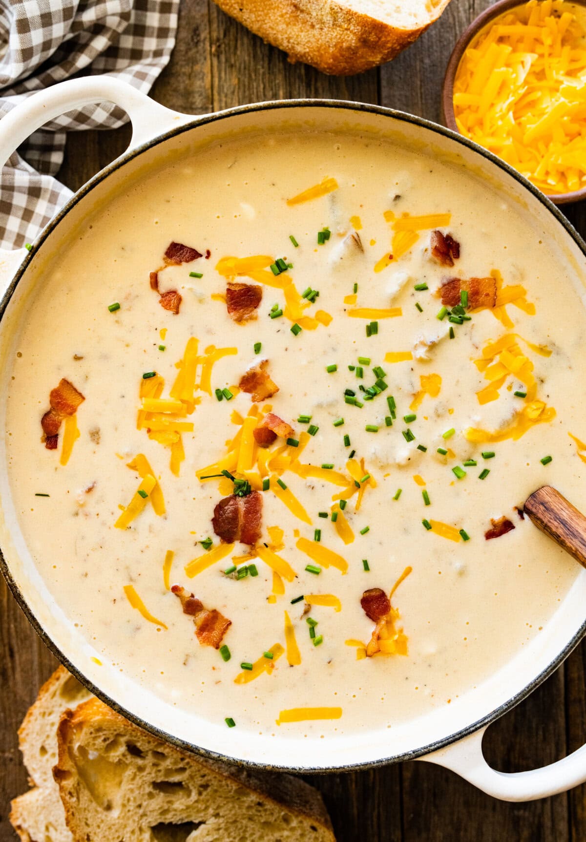 Wooden spoon in a Dutch oven of baked potato soup topped with cheese and bacon.