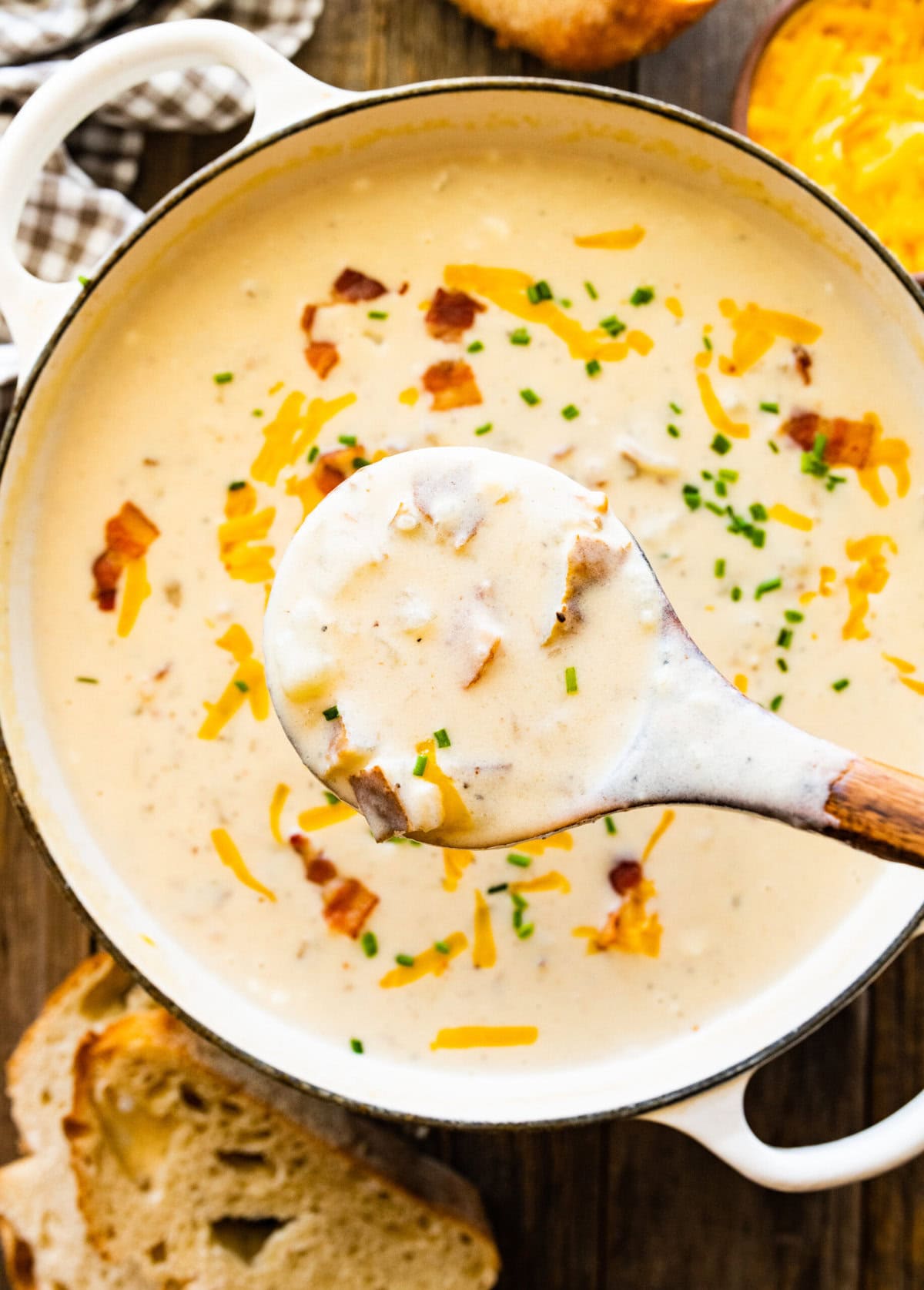 finished baked potato soup with a wooden spoon in it. Cheddar cheese and bacon bits on top. Wooden ladle and ready to serve.