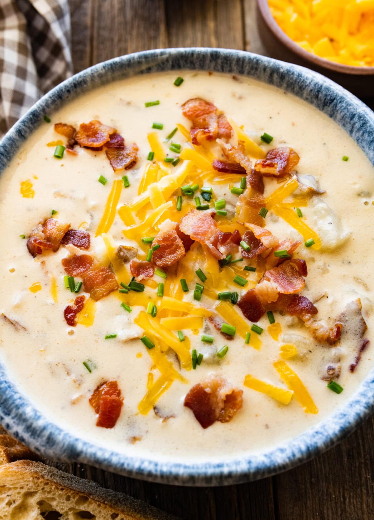 outback baked potato soup recipe in a bowl with a blue rim. Cheddar cheese and bacon bits on the top. Bread pieces on the side and napkin.