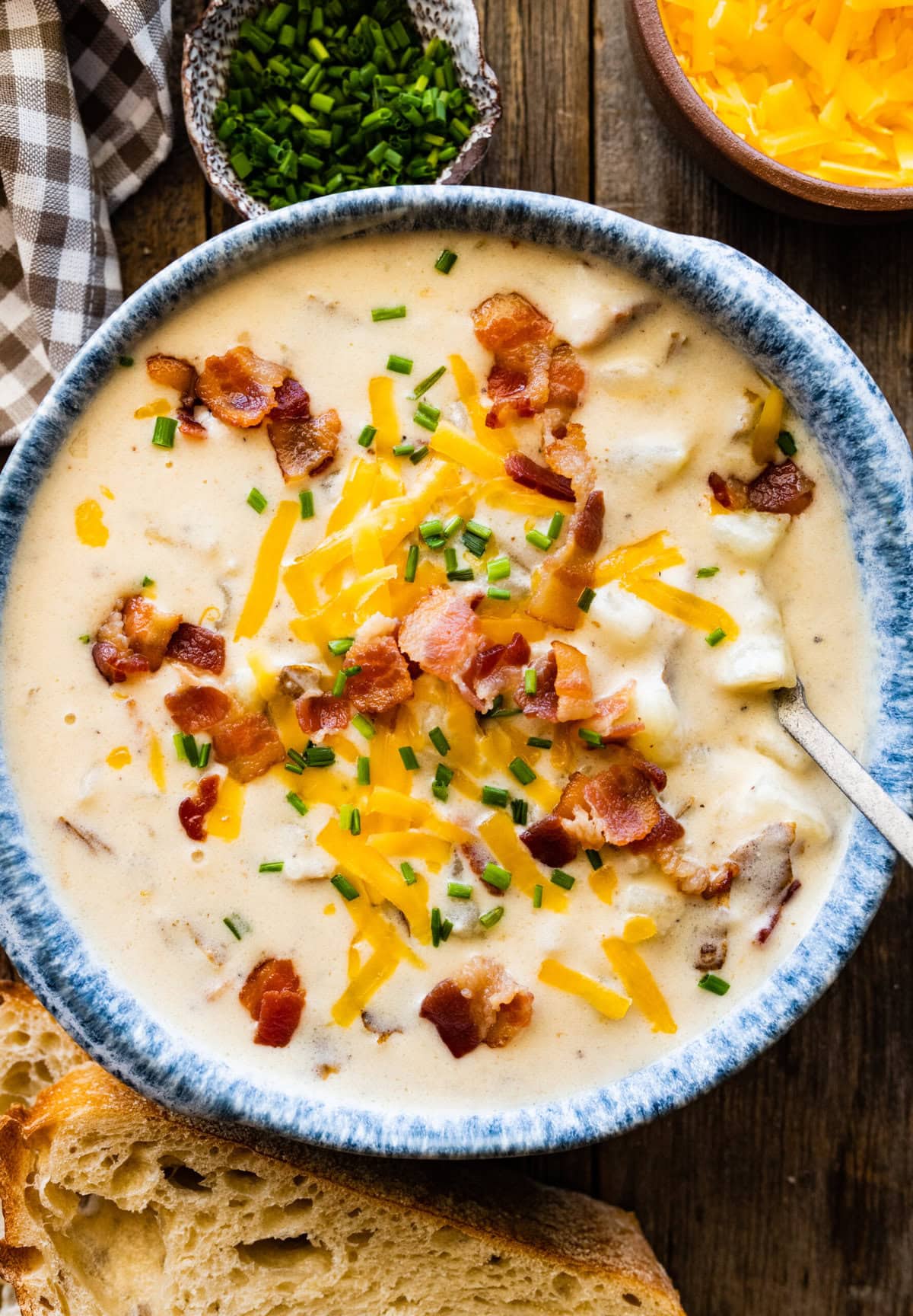 Spoon in a blue bowl of baked potato soup topped with cheese and bacon.