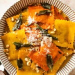 plated pumpkin Ravioli with Sage Brown Butter Sauce Recipe on a white plate. Served with parmigiano cheese on top.