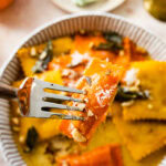 A fork holding up a bite of the plated pumpkin Ravioli with Sage Brown Butter Sauce Recipe on a white plate.
