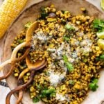 Beautifully plated charred corn and zucchini salad in a large serving bowl with ears of corn on the side and extra dressing. Mexican fresh cheese on top of the salad. Wooden salad servers on the side.