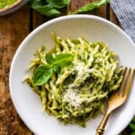 Fork on a white plate of pesto pasta.