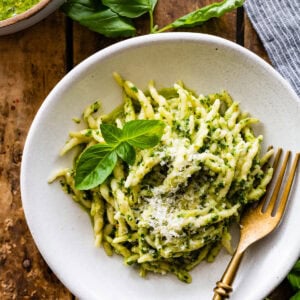 Fork on a white plate of pesto pasta.