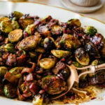 platted Brussels Sprouts with Bacon and Balsamic Recipe on a long white serving platter. Serving spoon on the platter ready to serve.