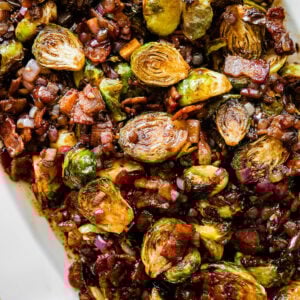 platted Brussels Sprouts with Bacon and Balsamic Recipe on a long white serving platter. Serving spoon on the platter ready to serve.