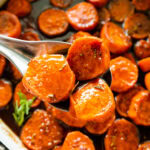 candied sweet potatoes after the are baked. Fresh herbs on top for garnish. Spoon holding up a portion serving.