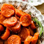 Candied sweet potatoes in a festive serving platter with a garnish of herbs.