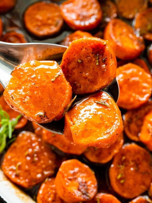 candied sweet potatoes after the are baked. Fresh herbs on top for garnish. Spoon holding up a portion serving.