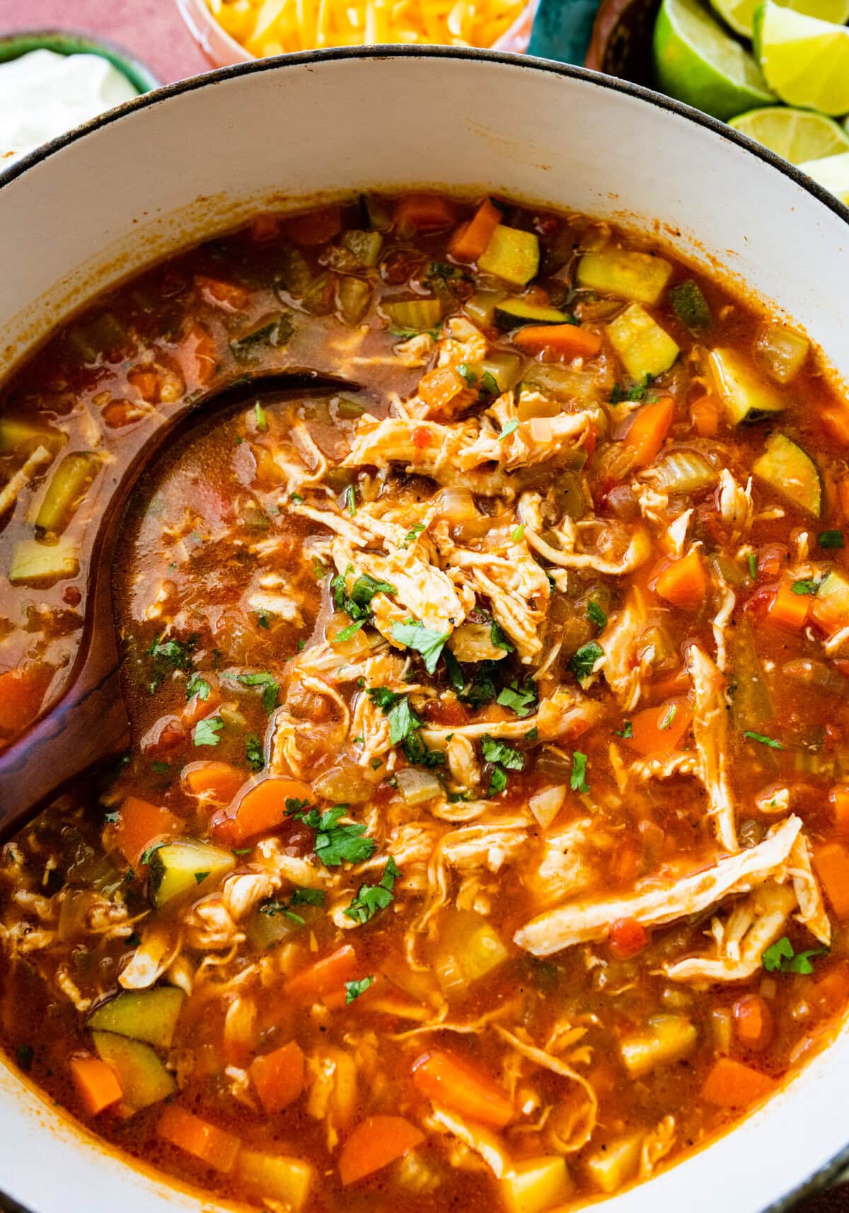 Easy Mexican chicken soup recipe with a large wooden spoon taking a serving.