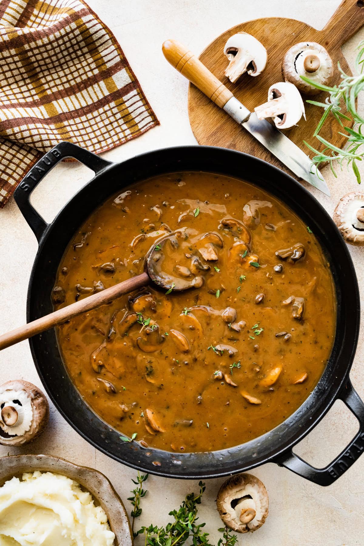 Easy mushroom gravy in a skillet pan with wooden spoon. Mushrooms on the side.