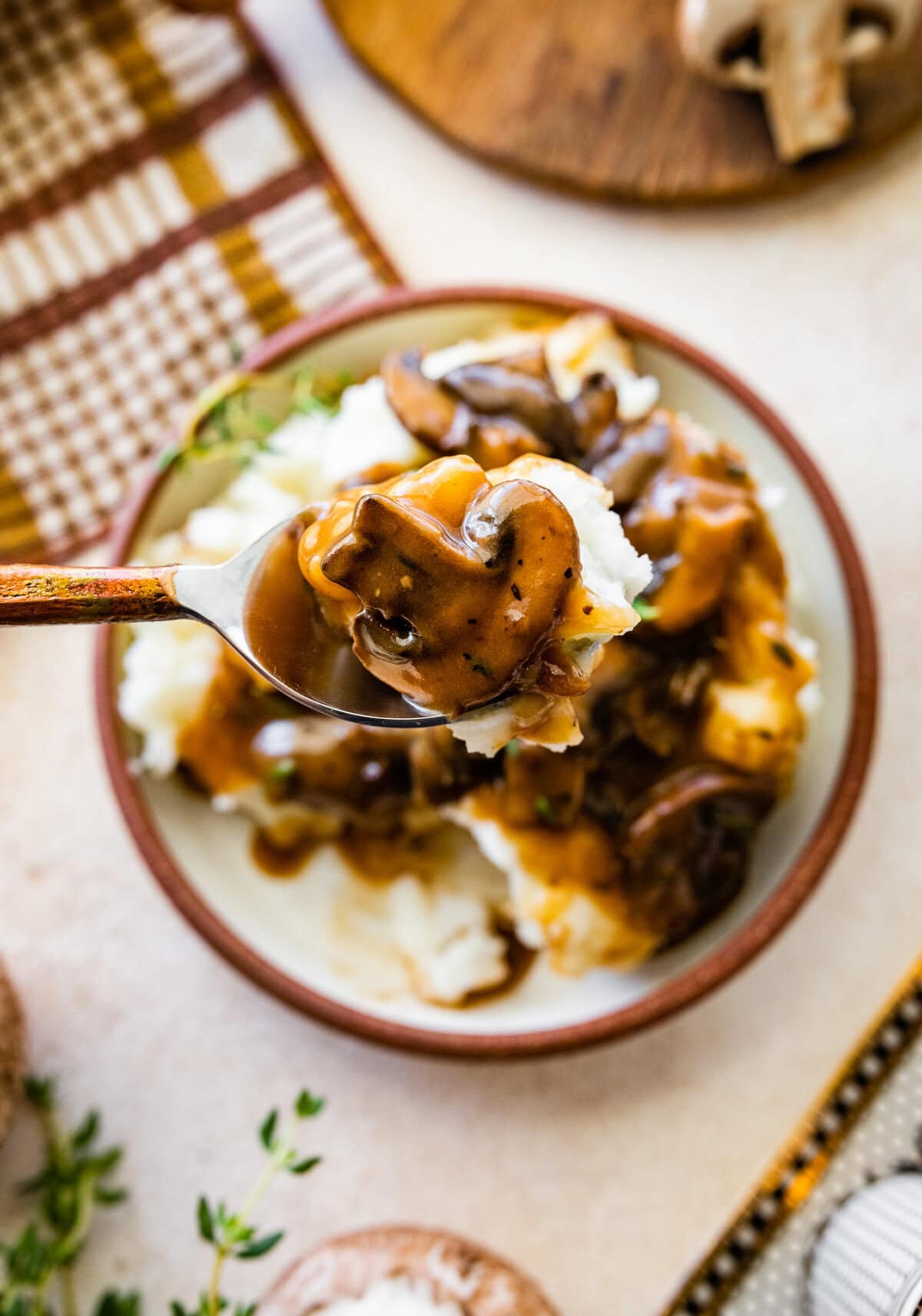 Easy mushroom gravy served over mashed potatoes and some herbs over the top. Spoon holding up a bite.