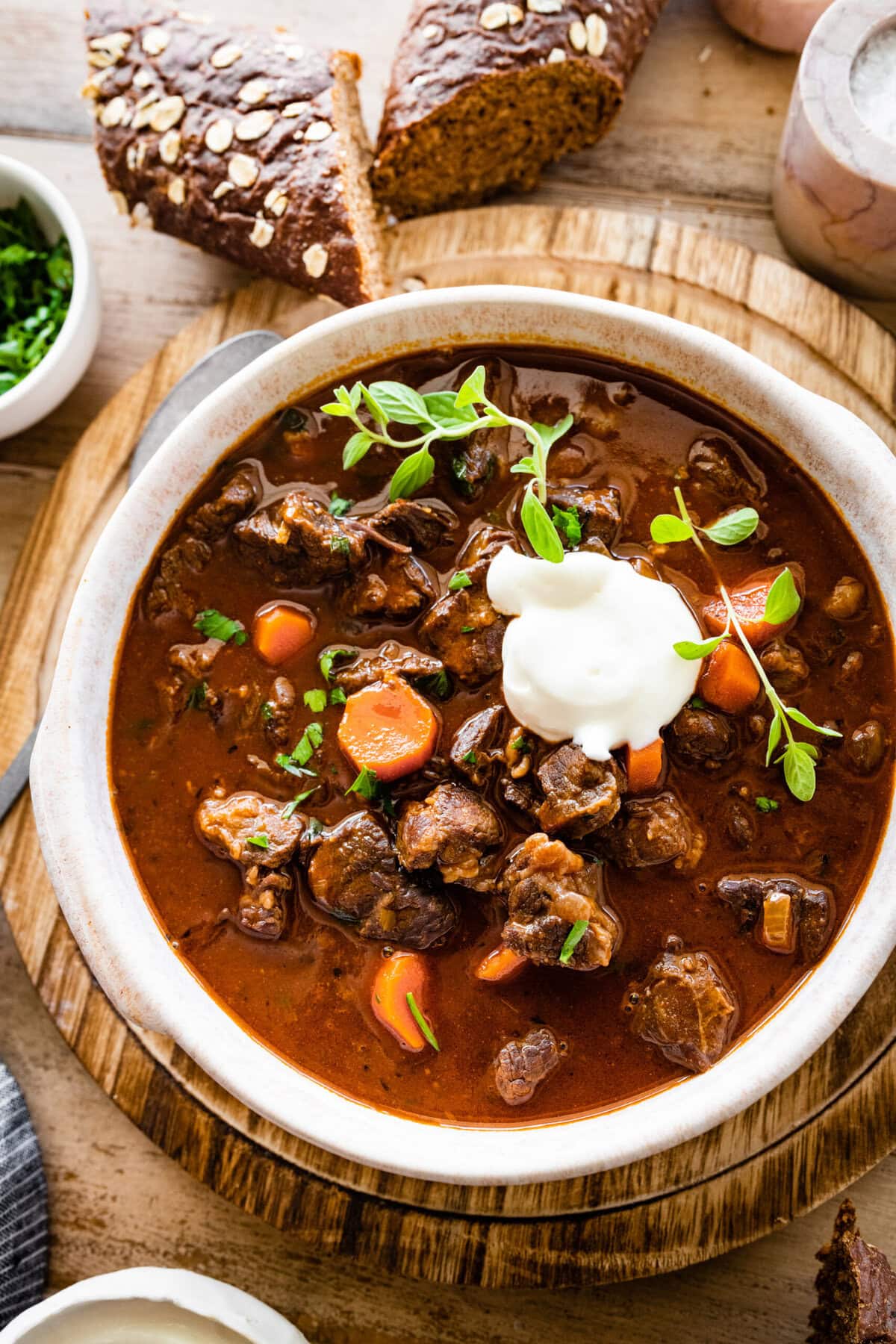 German Goulash Soup in a bowl with sour cream on the top and dark bread on the side. Spoon on the side.