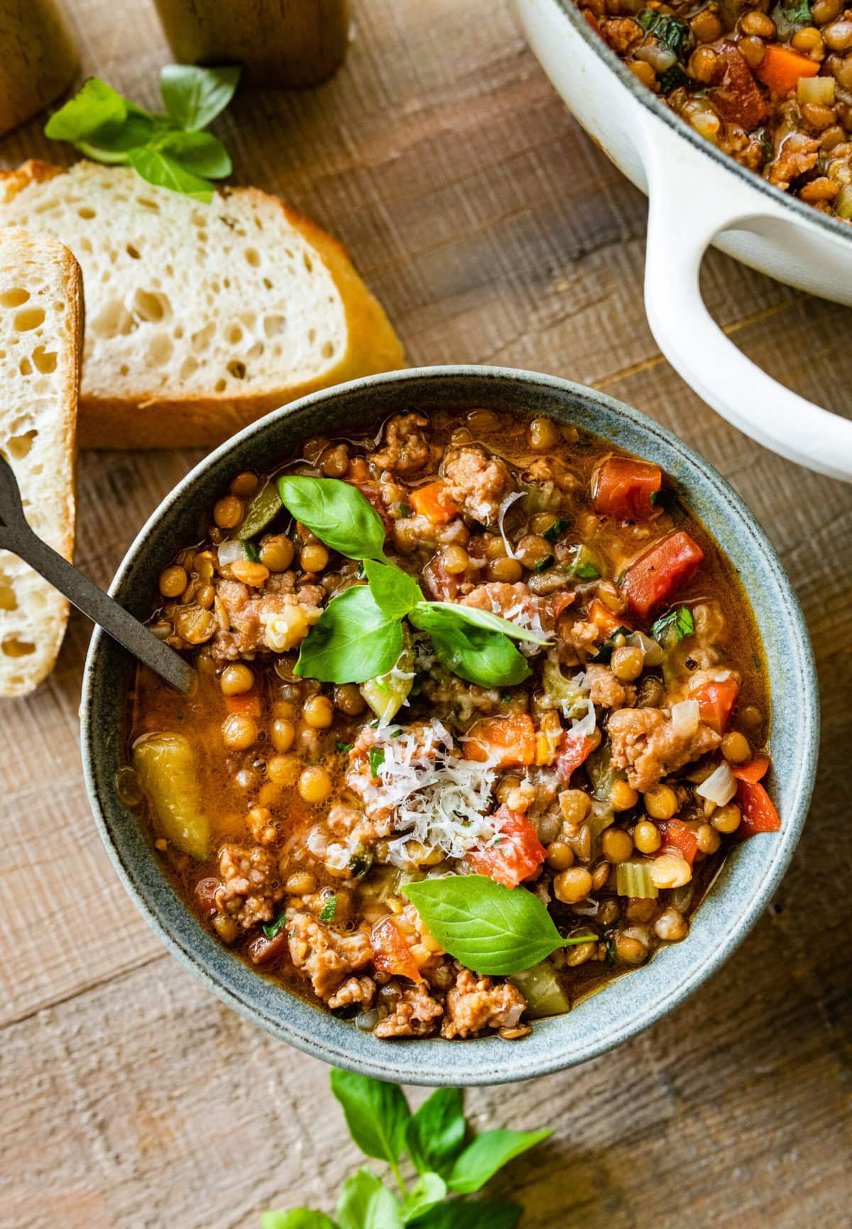 bowl of Italian sausage lentil soup recipe. Fresh parmigiano cheese and basil leaf as garnish.