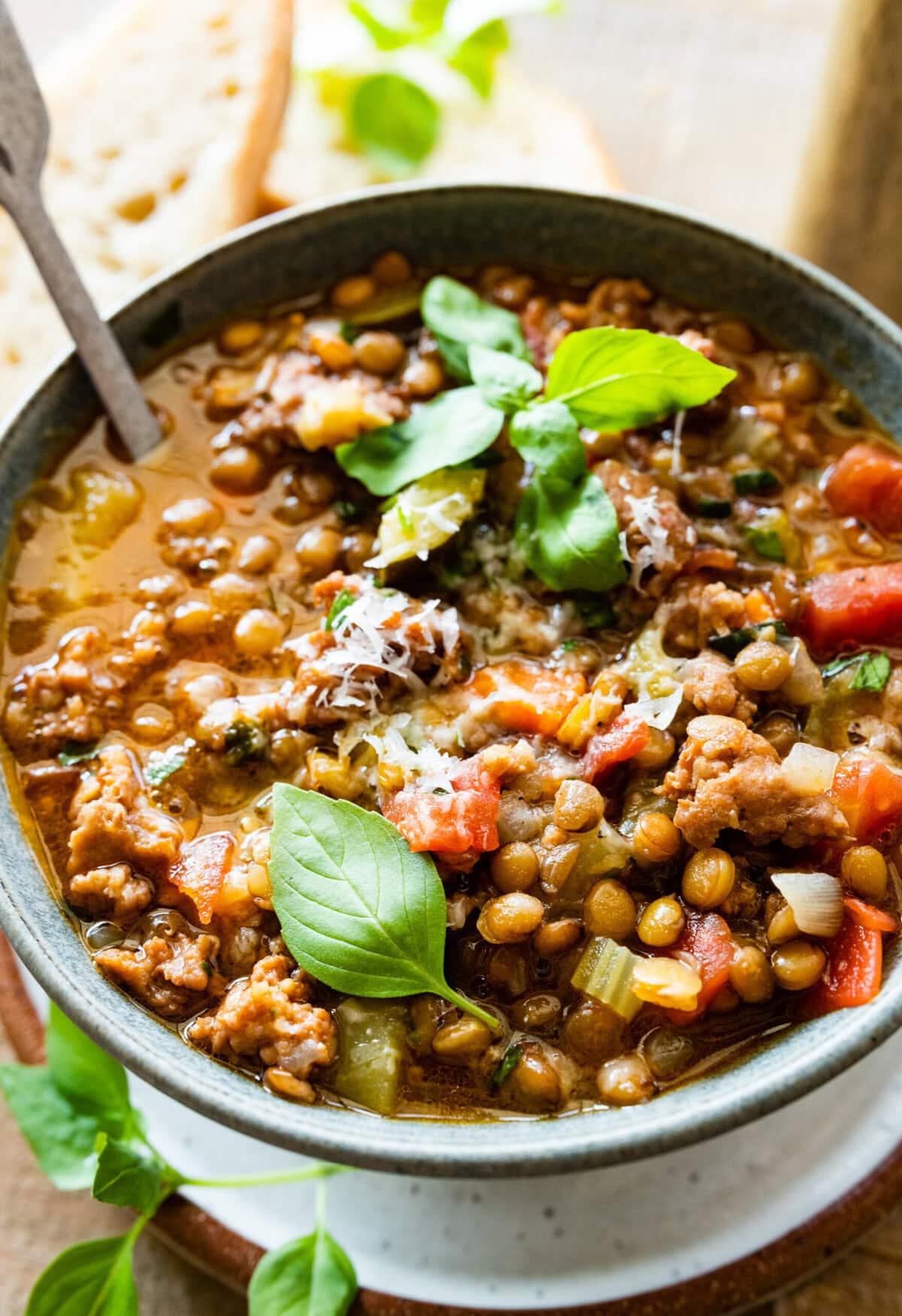 bowl of Italian sausage lentil soup recipe. Fresh parmigiano cheese and basil leaf as garnish.