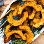 savory roasted acorn squash on a serving platter. Serving platter is white and blue with flowers. Garnish the plate with herbs.