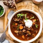 German Goulash Soup in a bowl with sour cream on the top and dark bread on the side.