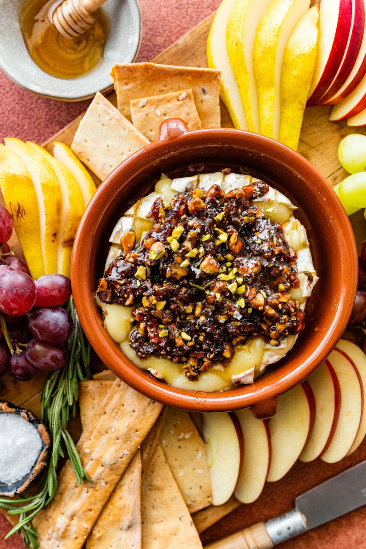 Beautiful baked brie with the topping on a platter with fruits, crackers, and a cheese knife to serve.
