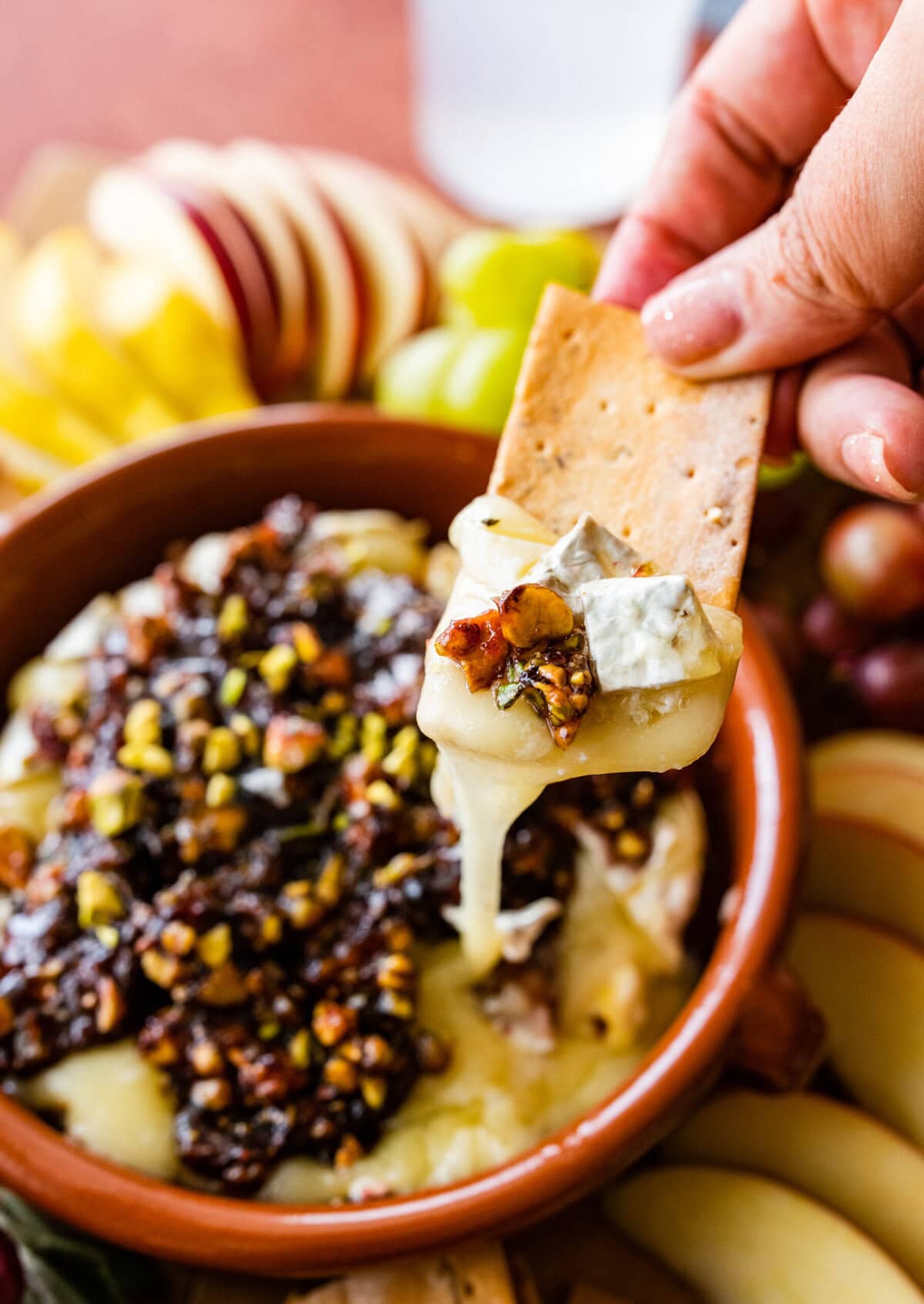 hand with a cracker taking a bite of the melty cheese with the savory jam and nut topping.