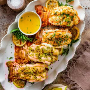 Best Baked lobster tails on a white serving platter with extra melted butter and lemon wedges for serving.