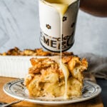 Pouring the warm vanilla sauce over the top of a bread pudding slice.