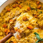 finished dish in the pot with sage on top. Wooden serving spoon in the pot. Spoon holding a portion of the orzo dish ready to serve.