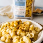 White bowl with easy cheese pasta sauce and crispy panko topping ready to eat with a fork. DeLallo Shellbow pasta package in the background to show brand.