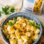Blue bowl with easy cheese pasta sauce and crispy panko topping ready to eat. DeLallo Shellbow pasta package in the background to show brand.