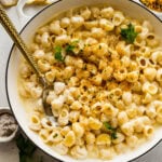 Cheese sauce for pasta in a skillet with shells and a wooden spoon.