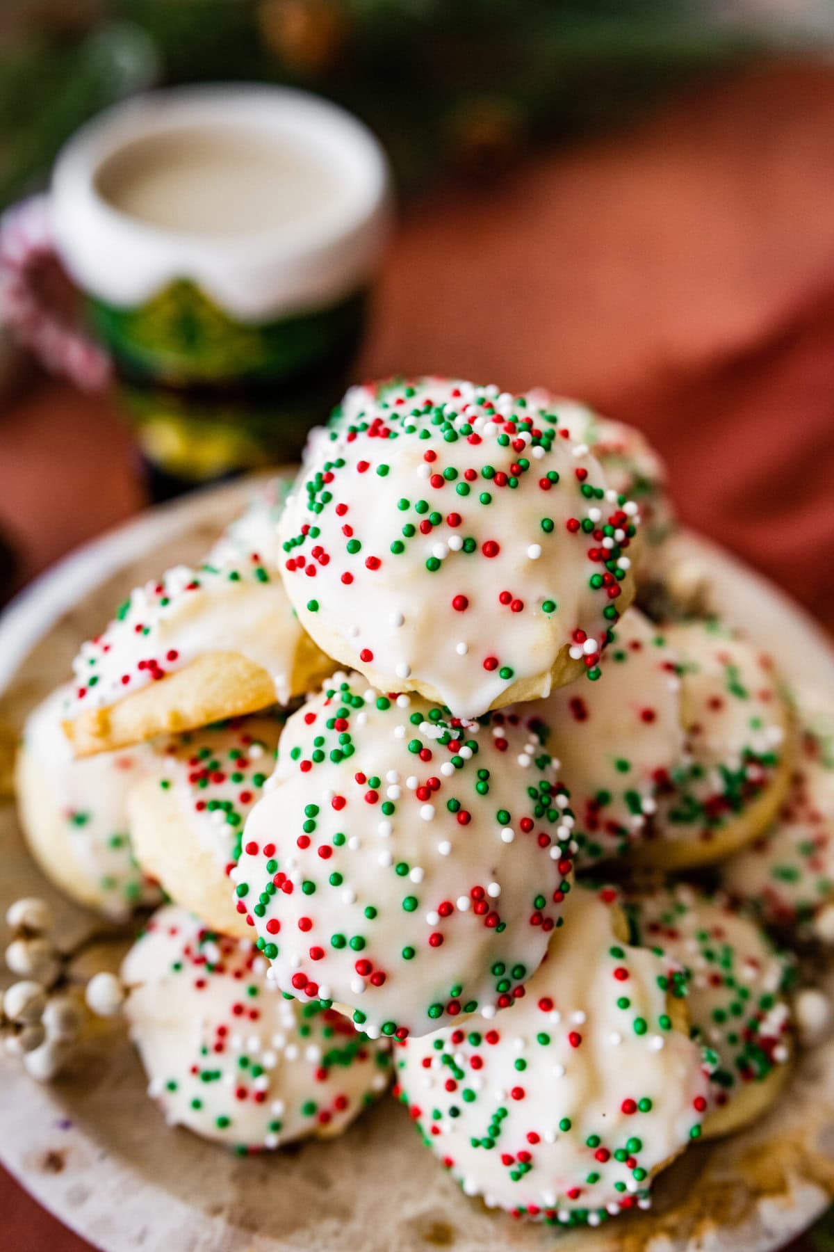 Pile of Italian Christmas cookies with white frosting and festive sprinkles surrounded by Christmas decorations.