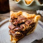 close up of a slice of baked Maple Pecan Pie (without Corn Syrup) on a white plate with a fork the pie plate is in the background.