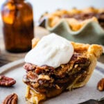 Slice of baked Maple Pecan Pie on a white plate topped with a dollop of whipped cream.