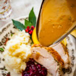 Pouring the turkey gravy over a plate of sliced turkey and mashed potatoes.