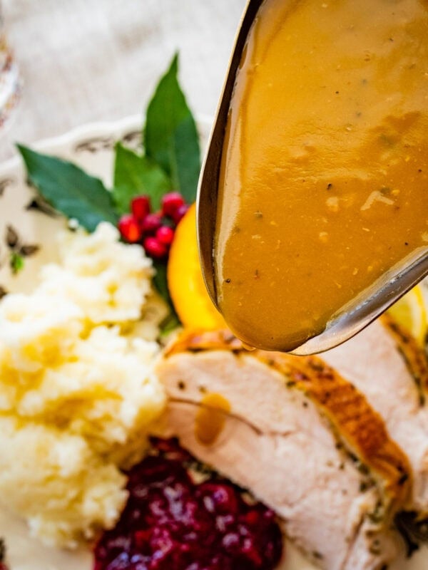 Pouring the turkey gravy over a plate of sliced turkey and mashed potatoes.