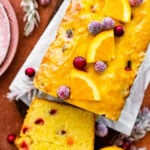 beautiful cranberry orange bread with orange glaze on a terracotta colored background. Oranges and sugared cranberries as decoration.