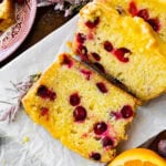 beautiful cranberry orange bread with orange glaze on a terracotta colored background. Oranges and sugared cranberries as decoration. Bread cut into slices to see the inside.