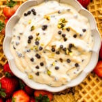 Easy cannoli dip in a bowl ready to serve on a beautiful platter with strawberries and pizzelle cookies as dippers. Optional pistachios on top for serving.
