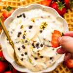 Person dipping a strawberry into a bowl of cannoli dip.